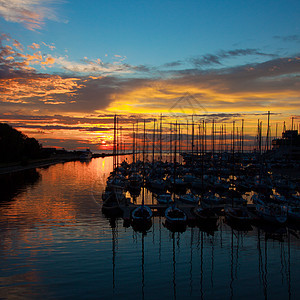 以日落时的游艇为港湾码头旅行海洋娱乐橙子镜子冒险太阳戏剧性桅杆图片