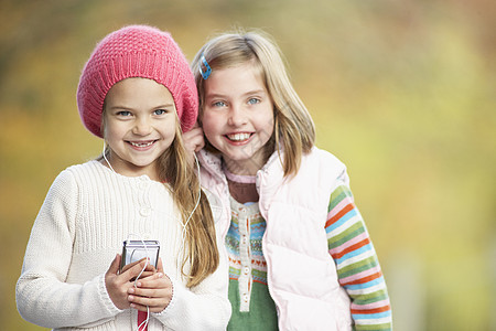 配有MP3播放器的两家年轻女孩户外游戏孩子女性朋友友谊音乐黑发针织品帽子农村耳机图片