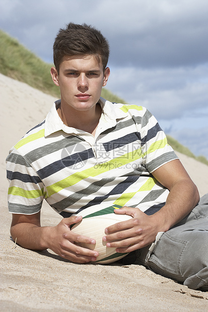坐在海滩上玩橄榄球的少年男孩青少年运动行动图片