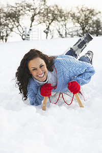 在雪地风景中的滑雪上骑车的年轻女子场景雪橇季节笑声帽子寒冷针织品爬坡女性场地图片