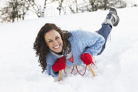 在雪地风景中的滑雪上骑车的年轻女子帽子混血场地季节农村笑声雪橇针织品雪人女性图片