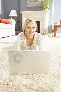 妇女在家里使用膝上型电脑轻松地躺在Rug上互联网地面冲浪笔记本成人闲暇娱乐客厅地毯微笑图片
