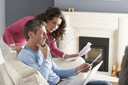 使用笔记本电脑和讨论家庭帐单的夫妇微笑账单男人办公休息室沙发客厅个人金融两个人图片