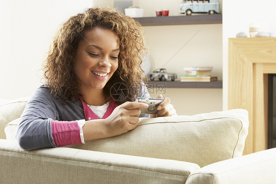 女性在数字摄影机上观看照片时的放松坐椅成人闲暇摄影沙发水平客厅长度娱乐相机微笑图片