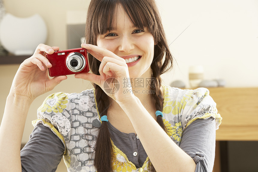 女青年在家里数码相机上拍摄摄影照片相机客厅长度爱好成人娱乐闲暇女性微笑水平图片