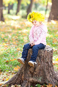 美丽的小姑娘 坐在石板上 坐着一朵满是青梅树叶的花圈里季节橙子乐趣童年快乐幸福孩子叶子公园树桩图片