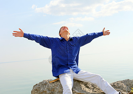 快乐的青年男子男人幸福天空乐趣蓝色微笑石头衬衫阳光岩石图片