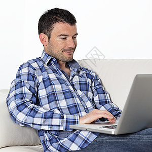 在沙发上放松男人电脑微笑青年互联网男性屏幕长椅软垫幸福图片