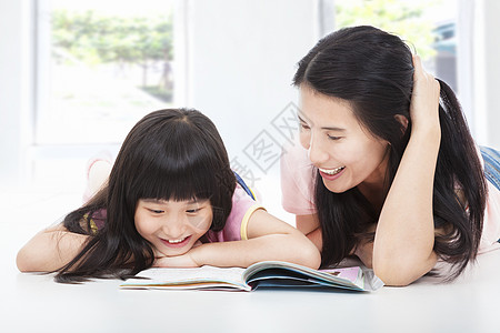 年轻母亲和女儿躺在地板上 看一本书图片