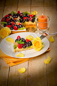 用蜡烛照亮的水果和花瓣薄荷甜点奇异果蛋糕浆果玫瑰桌木奶油糕点食物图片