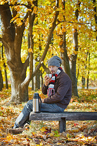 在秋天公园喝茶的人公园青年眼镜微笑男生帽子乐趣热水瓶树叶蓝色图片