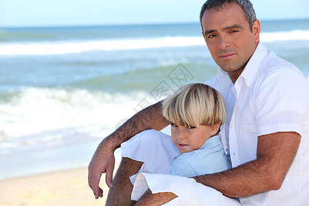 父亲和儿子坐在沙滩上享受家庭童年儿童男生快乐假期喜悦衣服微笑图片