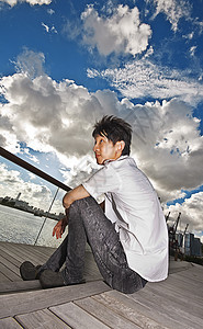 坐在公园里的亚洲人男人木头孤独港口蓝色天空商业旅游市中心牛仔裤图片