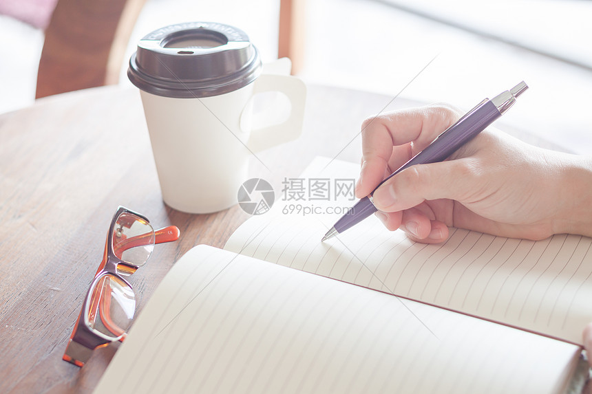 妇女写在笔记本上笔记软垫空白办公室咖啡文档桌子教育杯子木头图片