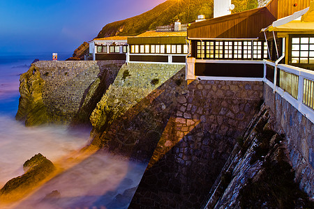 葡萄牙 日落时悬崖上的房子阳光海洋岩石酒店爬坡游客橙子窗户蓝色天空图片
