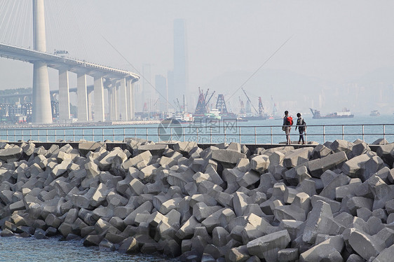 两人在防水堤上行走运输石头文化交通太阳旅行海洋天空集装箱曲线图片