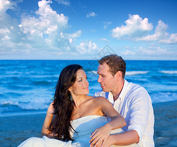 在蓝沙滩上坐着男人天空女士幸福波浪恋人新娘夫妻庆典蜜月图片
