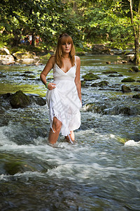 女孩跨水行走成人溪流假期裙子女士岩石树木旅行流动穿越图片