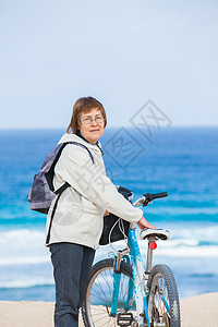 一位在海滩骑自行车的好高贵女士祖母运动微笑女性乐趣闲暇海洋活动娱乐骑术图片