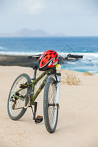 骑着头盔的自行车 站在海滩上浮木运动冒险阴影娱乐蓝色旅行海岸海洋戏剧性图片