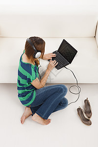 听音乐和使用笔记本电脑耳机沙发音乐导航黑发女孩享受房子技术乐趣图片