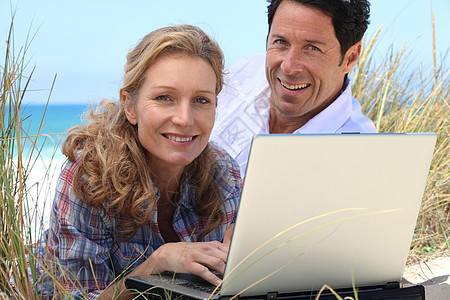 妻子在海滩上做笔记本电脑工作天空幸福头发丈夫男人女士棕色微笑白色个人图片