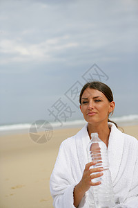 Brunette站在海滩上 拿着一瓶水图片