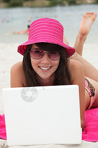 在海滩上用笔记本电脑 戴明亮粉红色帽子的年轻女人图片