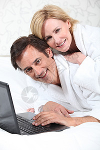 穿睡衣时在笔记本电脑上快乐的一对情侣微笑头发男性白色女性妻子男人棕色金发个人图片