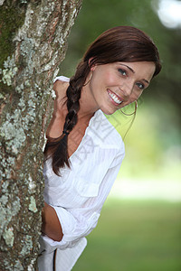微笑的女人 从树后面倾斜而出图片