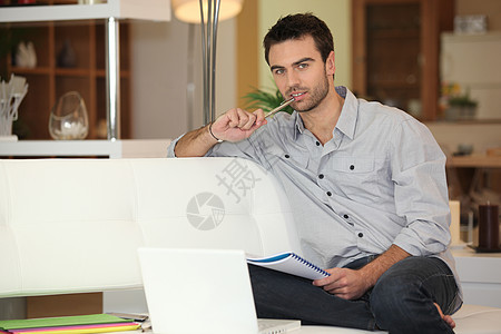 在笔记本电脑上工作的年轻人补偿男人冷却铅笔文件夹写作房子客厅衬衫沙发图片