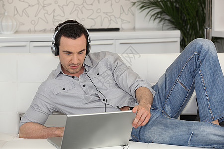 一个人用笔记本电脑和一对耳机躺在沙发上图片