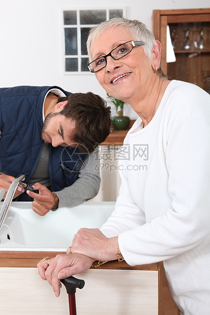 为一位年长妇女修理厨房水龙头的杂工图片
