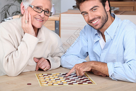 青年男子与年长妇女玩游戏女士跳棋游戏男人个人帮助微笑老年成人图片