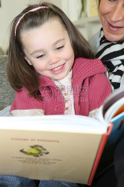 年轻女孩在成人帮助下阅读一本书图片