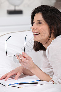 女人在床上写字头发棕色想象眼镜床罩女性听力毯子被子写作图片