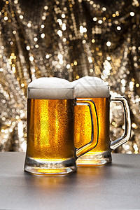 在闪闪发光的背景面前的啤酒杯啤酒厂金子啤酒饮料烧杯庆典背光派对闪光液体图片
