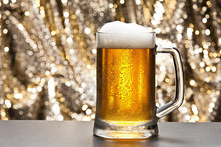 在闪闪发光的背景面前的啤酒杯金子草稿烧杯庆典派对玻璃静物豪饮液体泡沫图片