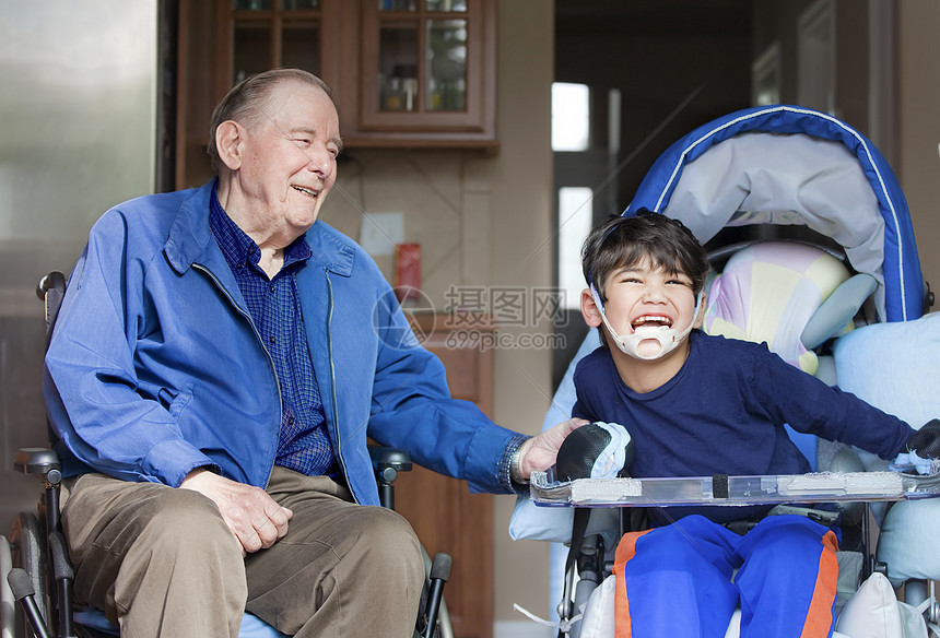 坐在轮椅上的老人男子与在厨房的残疾男孩一起笑图片
