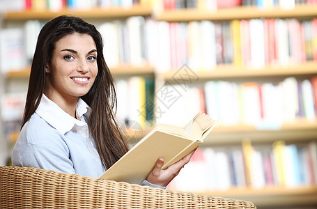 带着书在手的笑着微笑的女学生坐在椅子上教育校园青年文学大学书柜书架知识店铺图书馆图片