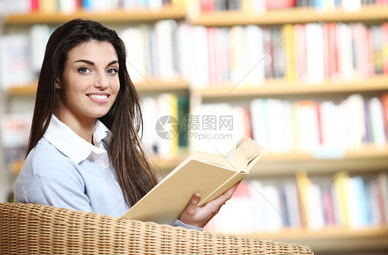 带着书在手的笑着微笑的女学生坐在椅子上教育校园青年文学大学书柜书架知识店铺图书馆图片