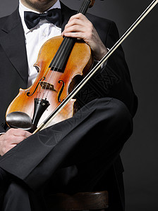 一个优雅的小提琴家 带着小提琴礼服衬衫深色晚礼服黑色木头古典音乐休息领结背景图片