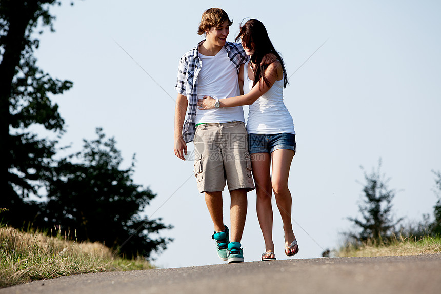 男女青年在夏季户外的一条公路上行走自由人行道友谊夫妻女士天空女孩场景沥青公园图片