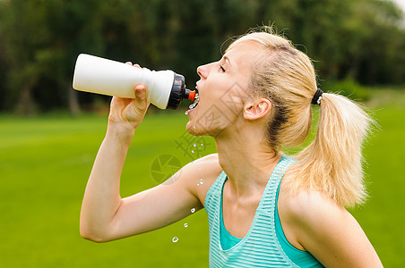 年轻女孩饮水饮用水赛跑者晴天女性公园蓝色女士口渴运动运动员瓶子图片