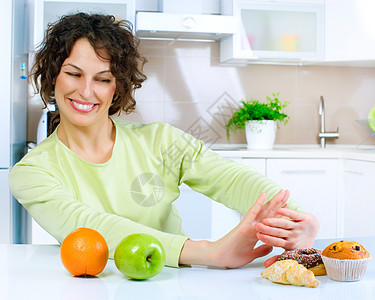 美丽的年轻女子在水果和甜甜之间选择甜点重量厨房诱惑女孩饮食损失身体思维早餐图片