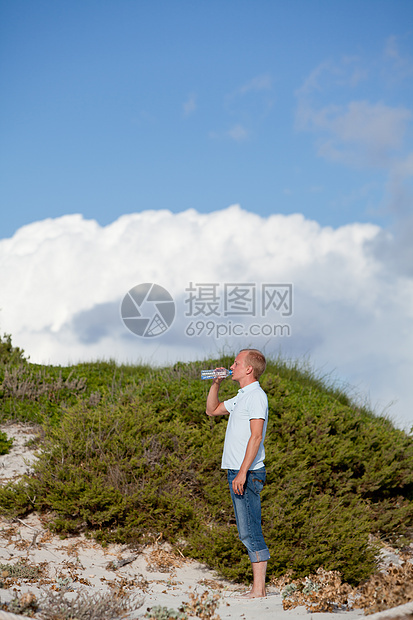 青年男子饮水夏日沙丘海滩天空沙丘成人海滩旅行男人液体微笑海洋蓝色饮料图片