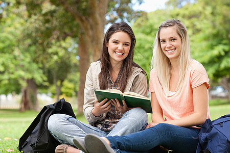 微笑的青少年在学习教科书时坐着图片