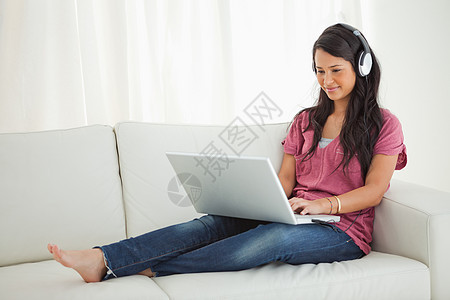 拉丁裔学生用笔记本电脑戴耳机微笑混血客厅沙发女性膝盖白色女士图片