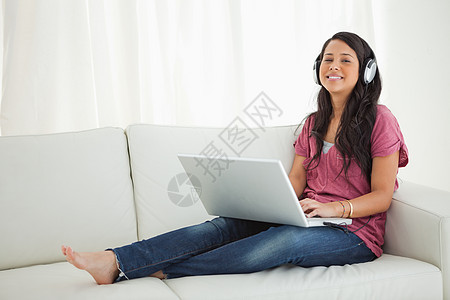 拉丁裔学生用笔记本电脑戴耳机白色微笑沙发膝盖女士混血女性客厅图片
