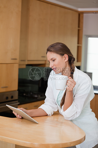 女人在看平板电脑时拿着杯子图片